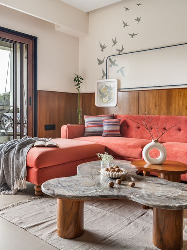 Living room with coral velvet sectional, walnut paneling, and a free-form stone coffee table