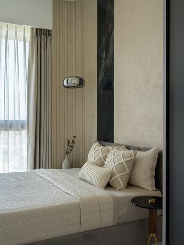 Corner of a beige bedroom with fluted panelling, sheer curtains, and a bed with textured cushions