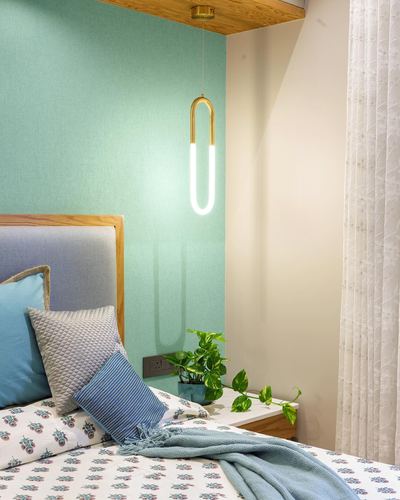 Bedroom corner with mint wall, brass U-shaped pendant light, and blue upholstered headboard with patterned linens