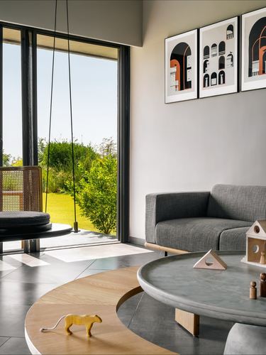 Living room with cane swing, grey sofa, round stone table and garden view through glass wall