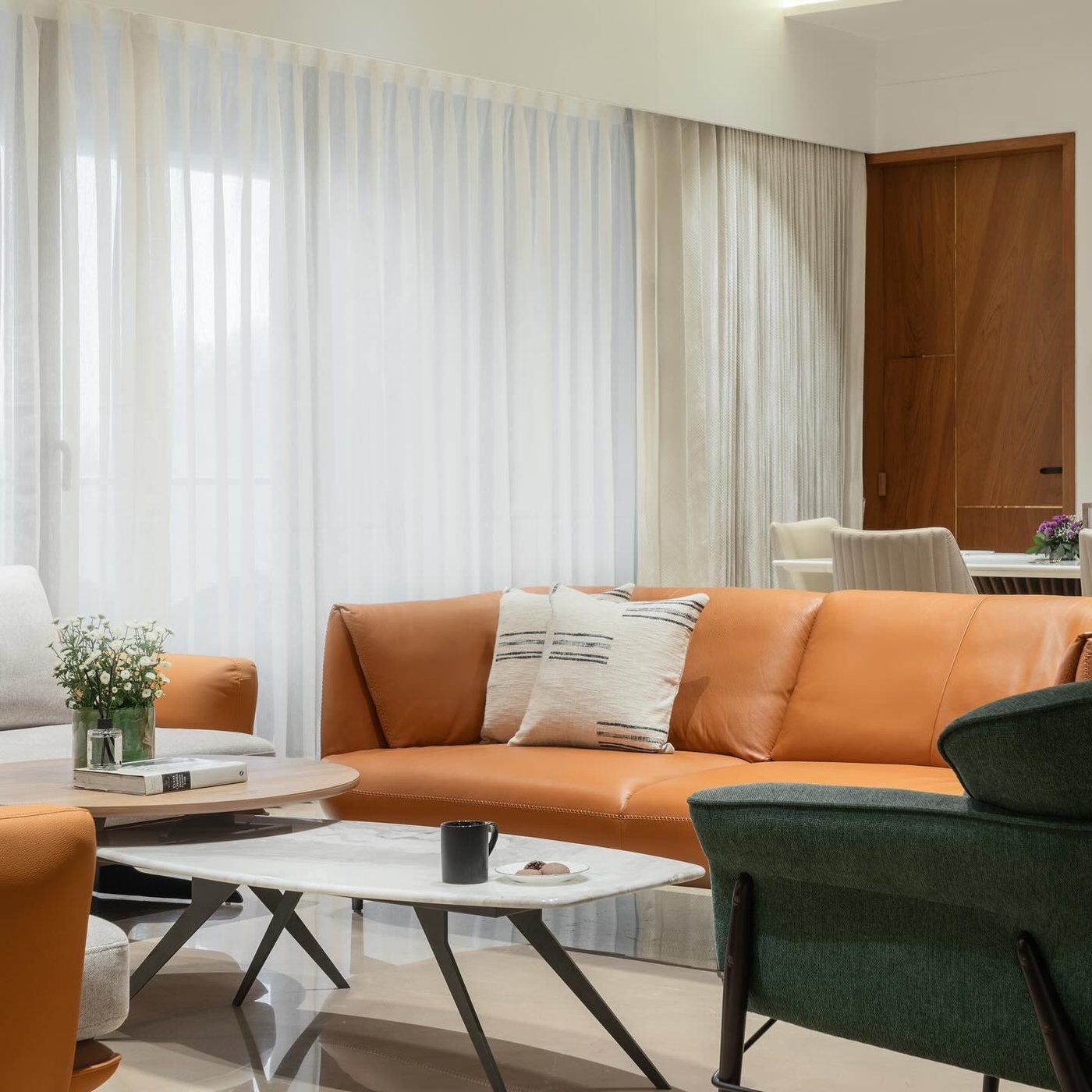 Living room with orange leather sofa, marble coffee table, sheer curtains and dining area beyond
