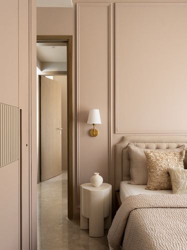 Pink-toned bedroom with paneled wall, brass sconce, and view through door to hallway