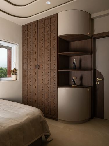 Bedroom with carved wooden wardrobe, curved shelving with figurines, and arched wooden door