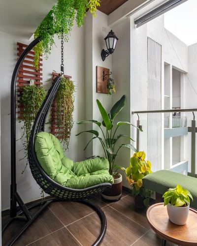 Balcony with black hanging swing chair, green cushions, trailing plants and wood trellis panel