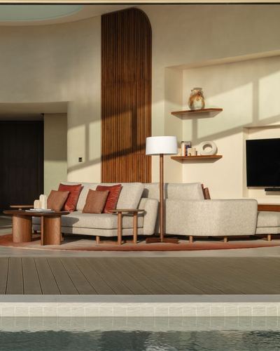 Living area with beige sofa, terracotta cushions, fluted wood panel, and pool deck in foreground