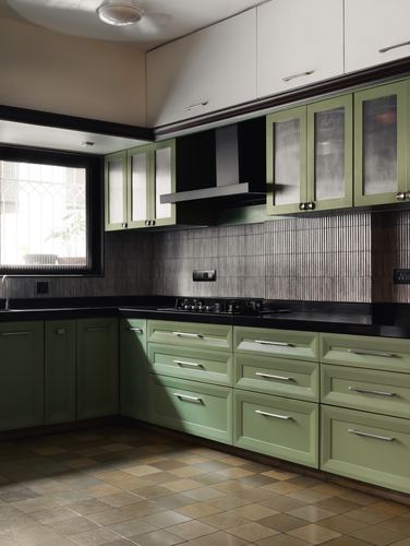 L-shaped sage green kitchen with black countertop, ribbed metallic backsplash, and terracotta floor tiles