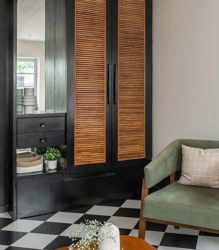 Black cabinet with wooden louvre doors beside green sofa on checkerboard floor