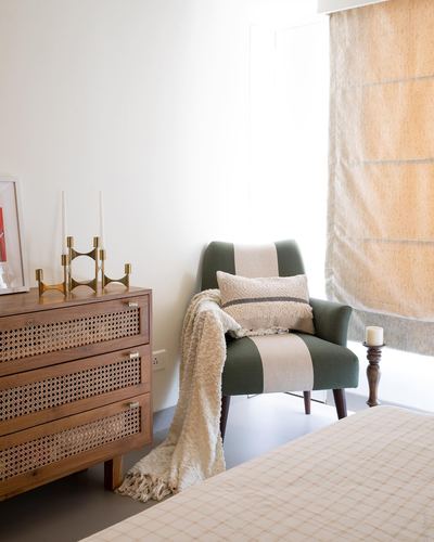 Bedroom corner with cane dresser, brass candelabra, and green striped armchair by window