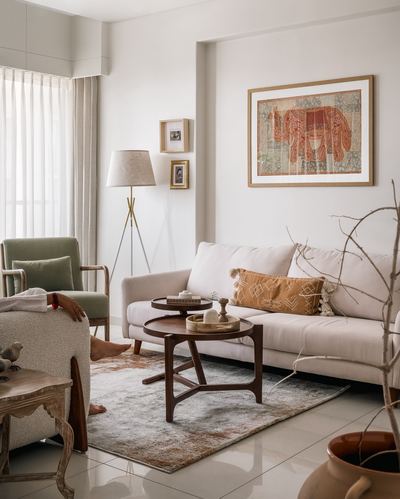 Neutral living room with sage armchair, cane sofa, round wood tables and elephant tapestry