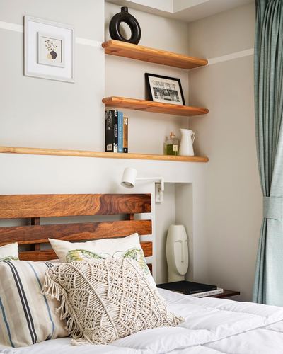 Slatted wood headboard beneath floating wood shelves with books and ceramics in neutral bedroom
