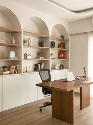 Home office with three arched wooden shelving niches and a wooden desk with black chair