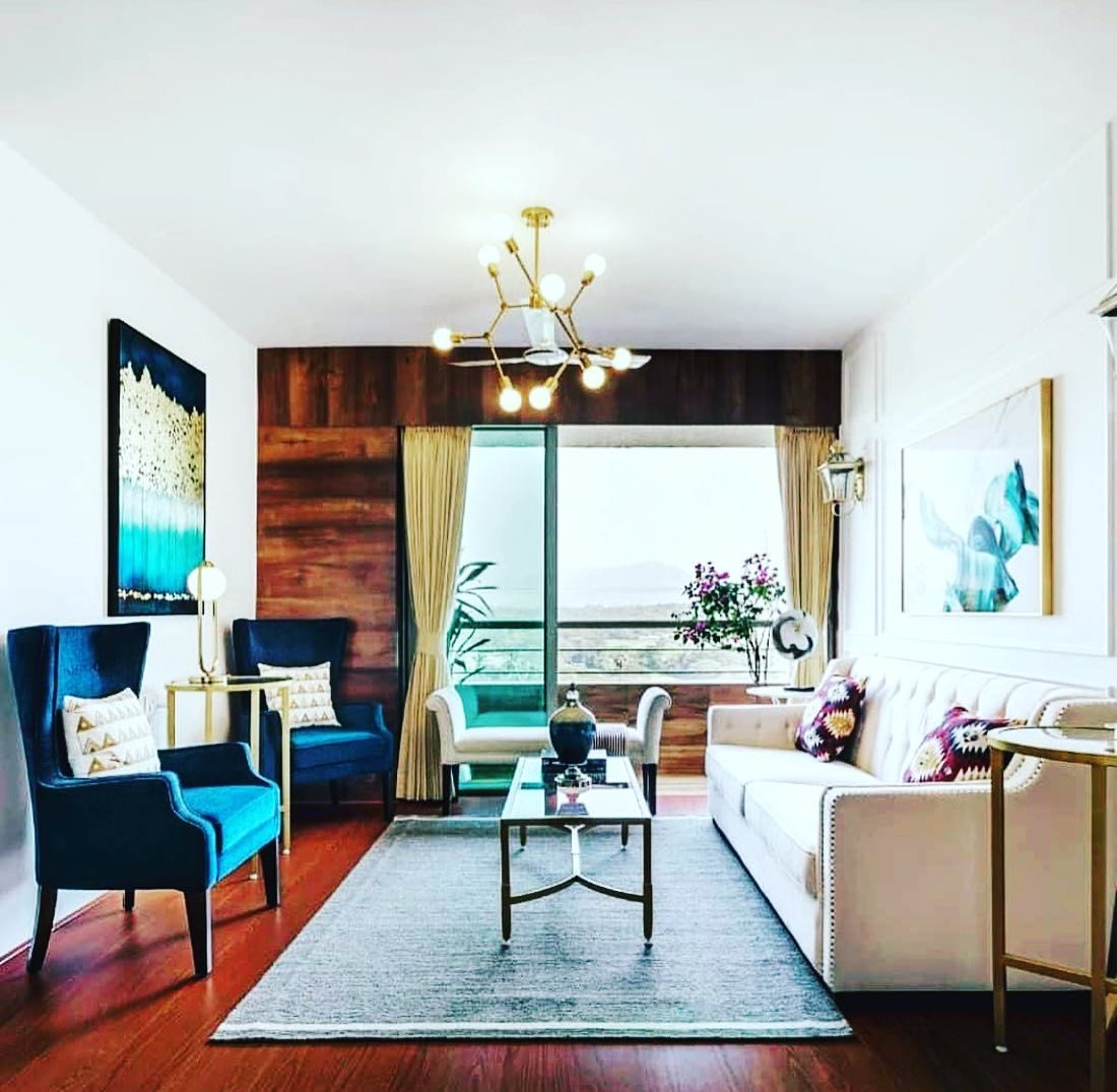 Living room with blue wingback chairs, cream sofa, and wood accent wall opening to balcony