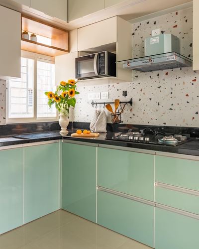 L-shaped mint green modular kitchen with terrazzo backsplash and sunflowers on black countertop
