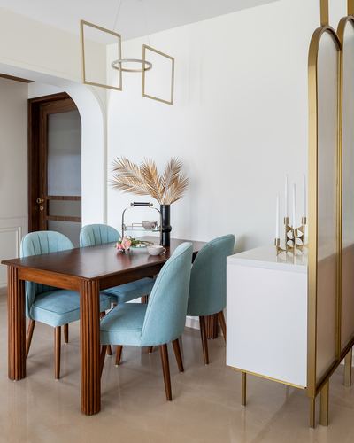 Dining room with fluted wood table, teal velvet chairs, and gold arched room divider