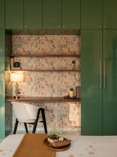 Study nook with floral wallpaper, wood shelves, desk lamp, flanked by glossy green wardrobes