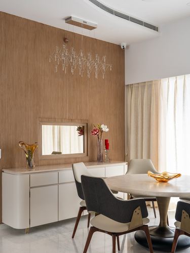 Dining area with fluted wood wall, sideboard, mirror, chandelier and round marble table