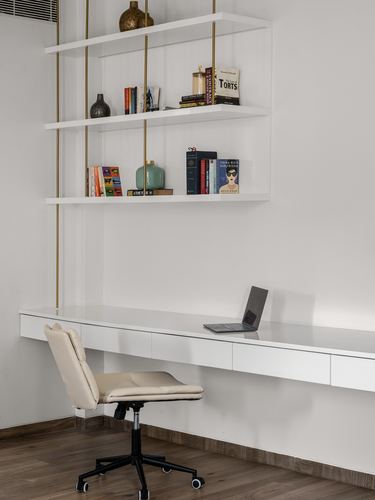 White floating desk and shelving unit with brass rod supports, beige office chair, laptop on desk