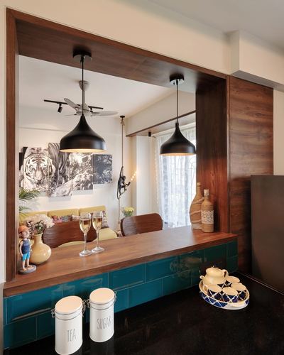 Wood-framed kitchen counter with teal tile front, black pendant lights, dining area beyond