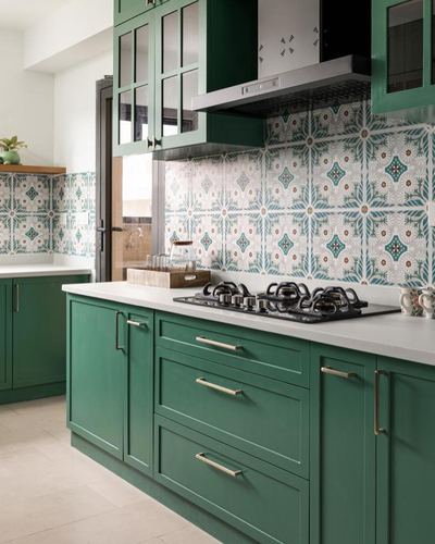 Green kitchen cabinetry with patterned tile backsplash, white countertop, and black gas hob under a chimney hood