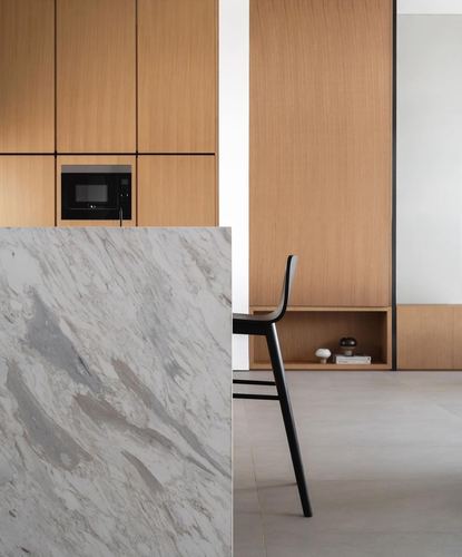 Modern kitchen with veined marble island, wood cabinetry, and black bar stool