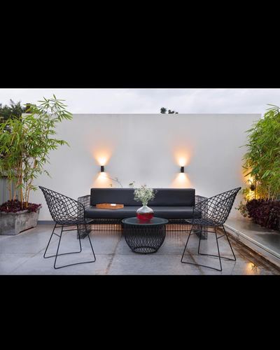 Rooftop terrace with black wire chairs, dark sofa and glass table lit by two wall sconces