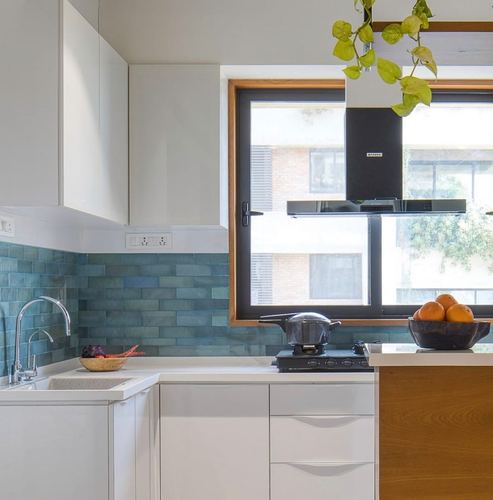 White kitchen corner with blue subway tile backsplash, black chimney hood, and wood-fronted island under a window