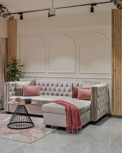 Beige tufted L-shaped sofa with pink cushions against arched paneled wall, wood slat columns, track lighting