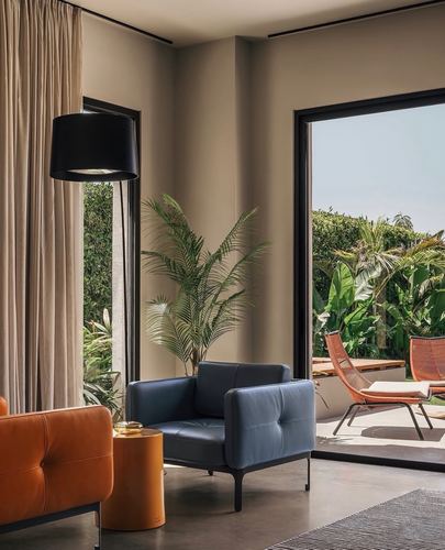 Living room corner with orange and navy leather armchairs facing floor-to-ceiling windows onto a green terrace