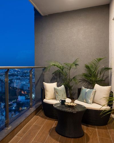 Balcony with wicker chairs, glass table, palms and city skyline at dusk
