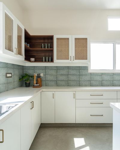 White kitchen corner with cane-front cabinets, green tiled backsplash, and open wood shelving