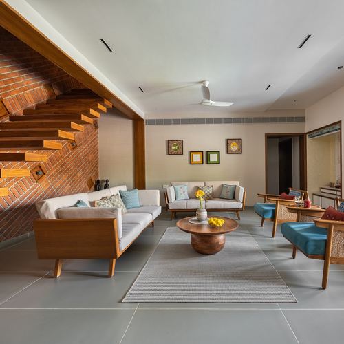 Living room with exposed brick staircase, wooden sofas, and grey stone flooring