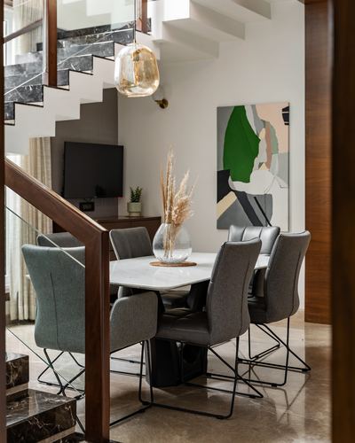 Dining table under staircase with amber pendant light and abstract green painting on wall