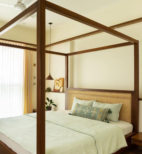 Wooden four-poster bed with cane headboard and sage linens beside a curtained window