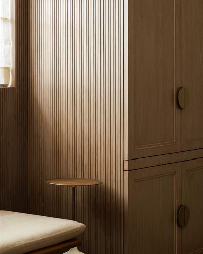 Fluted wood-panelled corner with round brass side table beside a wardrobe with circular pulls