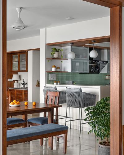 View through wooden doorway into dining area and open kitchen with green tiled counter and rope bar stools