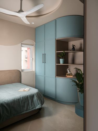 Bedroom with curved blue wardrobe, open shelves, ceiling fan, and arched window above bed