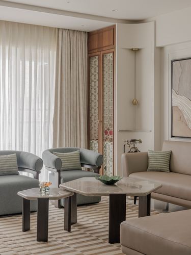 Living room with sage armchairs, hexagonal stone tables, and a jaali-front cabinet niche