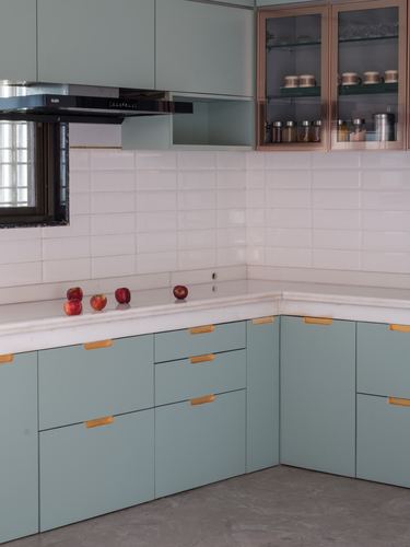 L-shaped kitchen with sage cabinetry, white subway tile backsplash and brass-trimmed glass cabinet