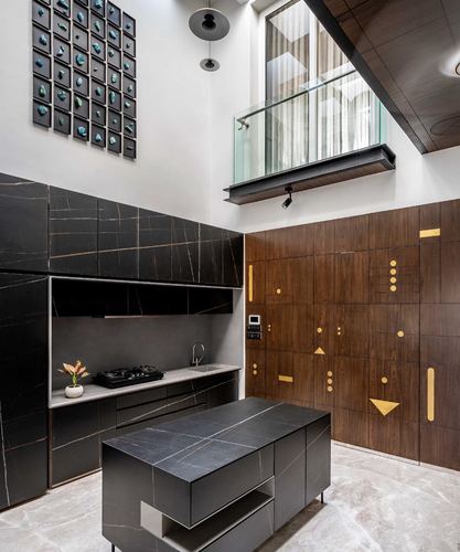 Double-height kitchen with dark stone island, inlaid wood wall, and glass balcony above