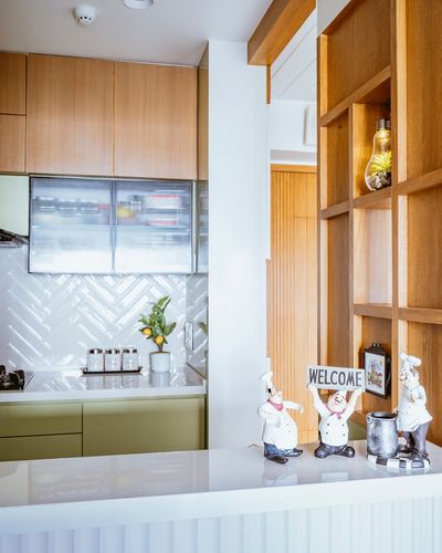 Kitchen counter with chef figurines and welcome sign, herringbone tile backsplash, wood cabinetry beyond