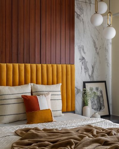 Bedroom with wood-slat wall, mustard velvet headboard, layered pillows, marble accent wall and globe pendants
