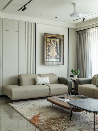 Neutral-toned living room with fluted panelling, framed deity artwork, leather sofas, and marble floor
