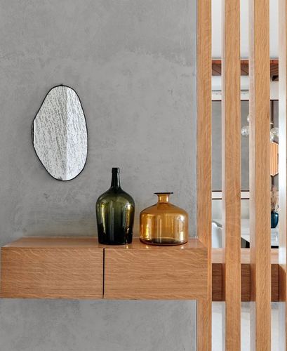 Floating wood console with mirror and glass bottles against textured grey wall, wood slat divider beside it