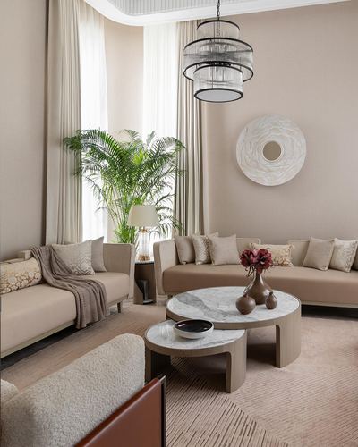 Beige living room with curved sofas, nested round tables, and a layered drum chandelier