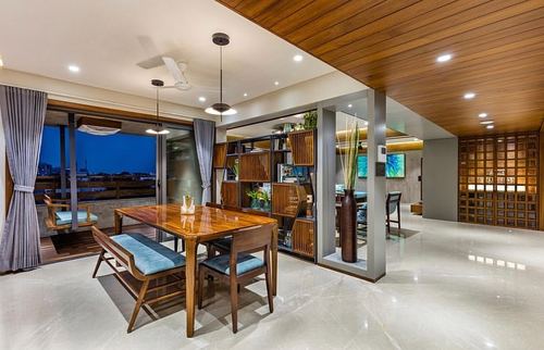 Wood dining table with blue-cushioned bench under pendant lights beside a slatted partition