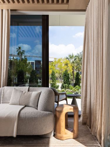 Cream boucle sofa and carved wood stool beside sliding glass doors overlooking a landscaped garden
