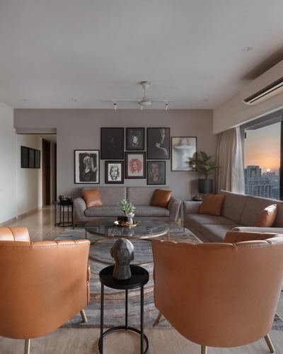 Living room with tan leather chairs, grey sofas, gallery wall, and city view at dusk