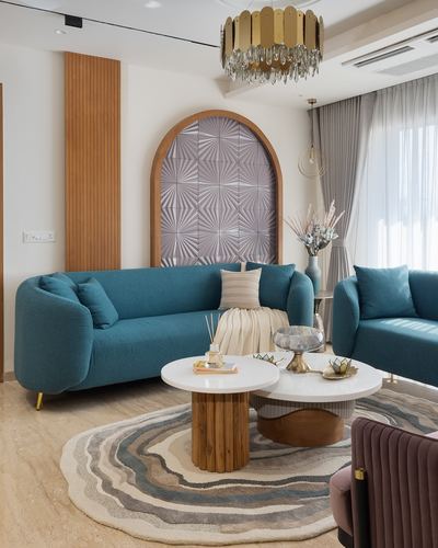 Living room with teal sofas, arched textured wall panel, brass chandelier and round wood coffee tables