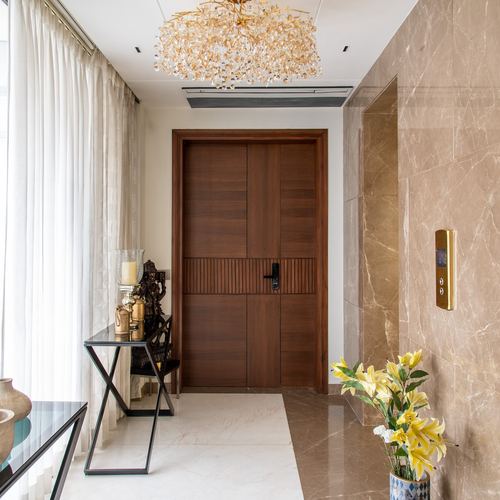 Marble-clad foyer with dark wood double door, crystal chandelier, and glass console table