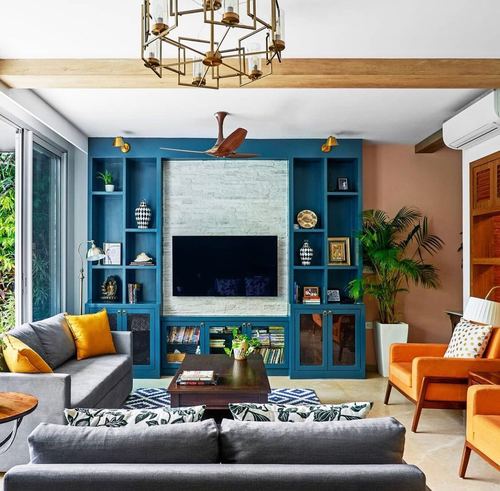 Living room with teal built-in TV unit, stone panel, orange chairs and grey sofas